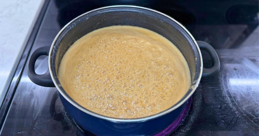 Homemade Apple Cider Salted Caramel Recipe coming to a boil in a large blue pot.